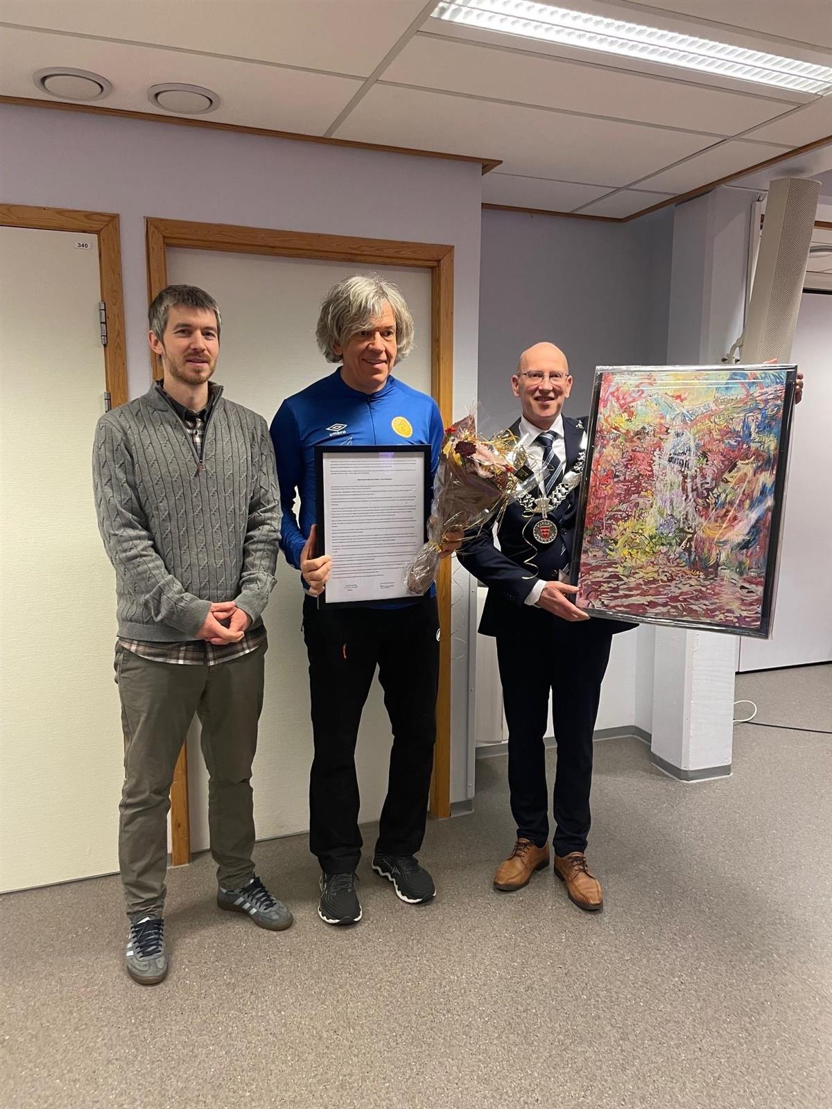 Foto som viser leiar i Fjalerpriskomiteèn, ordførar og prismottakar Jonny Pedersen som held fram kunstverk av Nikki De Marco - Klikk for stort bilete